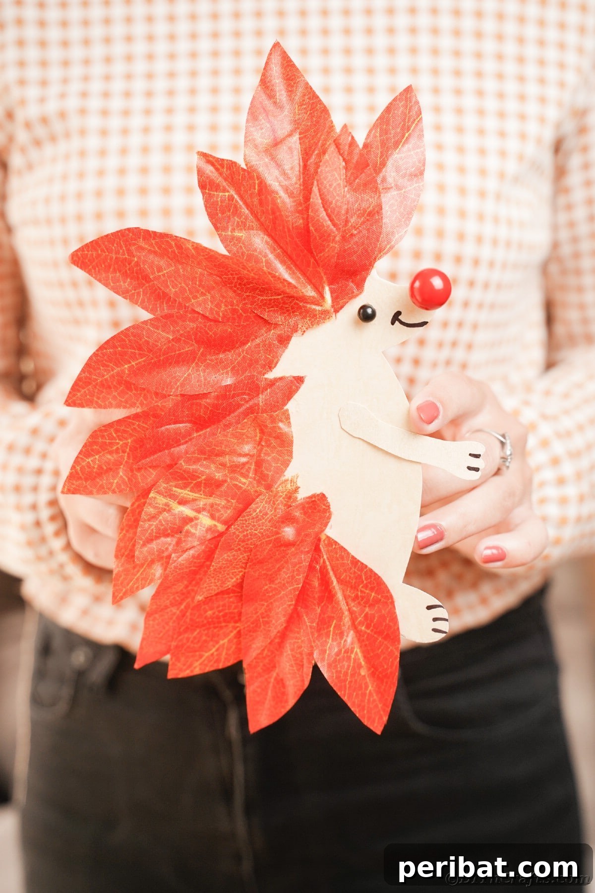 Woman in black pants holding paper hedgehog in front of her, showing scale.