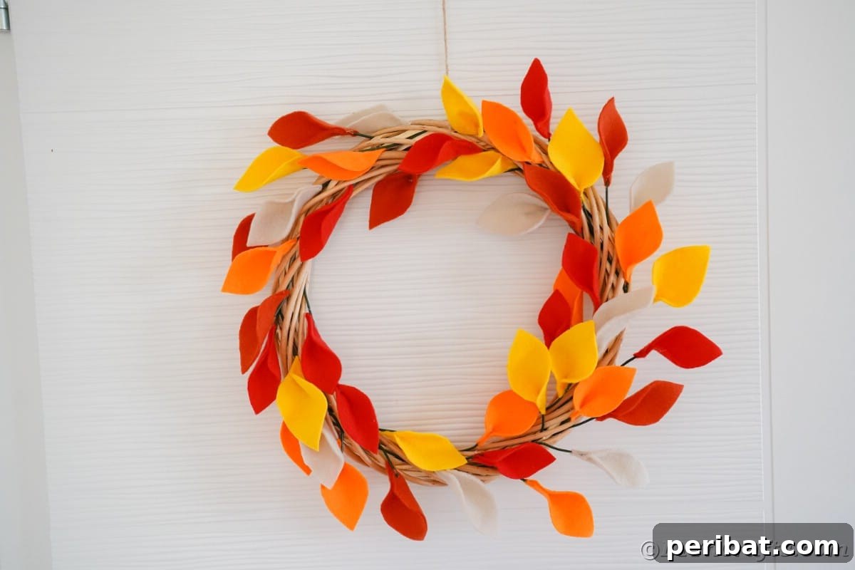 Orange and yellow fake leaves on grapevine wreath hanging on white door