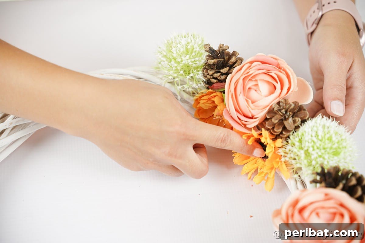 Charming Fall Blossom & Pinecone Wreath 9 Hands holding flowers in place on wreath