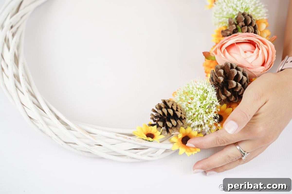 Charming Fall Blossom & Pinecone Wreath 10 Hand putting sunflowers on white wreath by pinecones