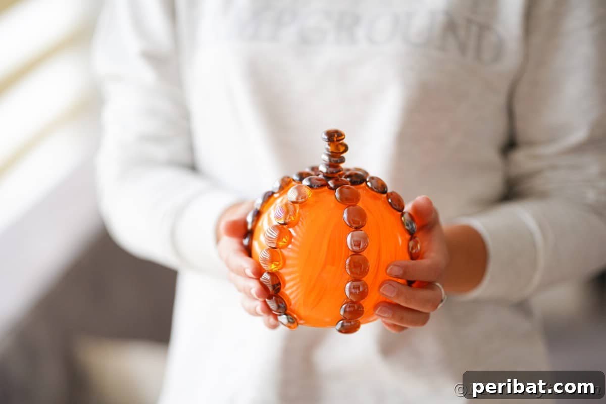 A woman in a white sweater gently holds the finished glass pumpkin, showcasing its delicate design and inviting warmth.