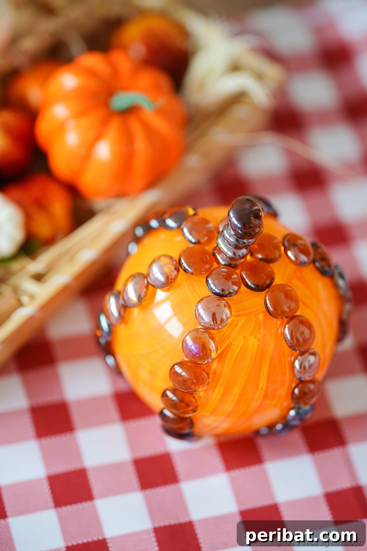 A beautifully painted glass fishbowl pumpkin sits as a centerpiece on a table adorned with a festive red checked tablecloth, exuding rustic charm and seasonal warmth.