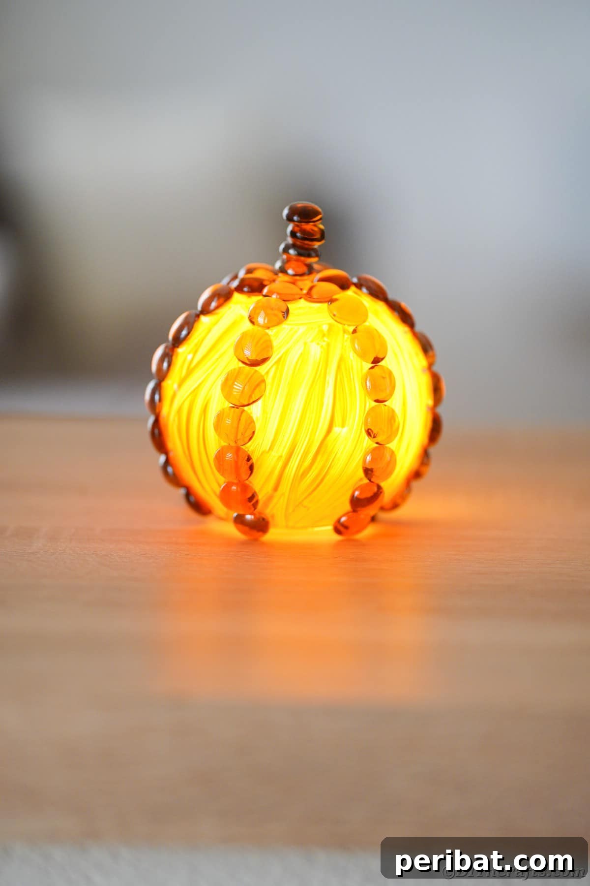 A beautifully painted glass pumpkin sits on a table, subtly illuminated by an LED candle placed inside, highlighting its festive glow.