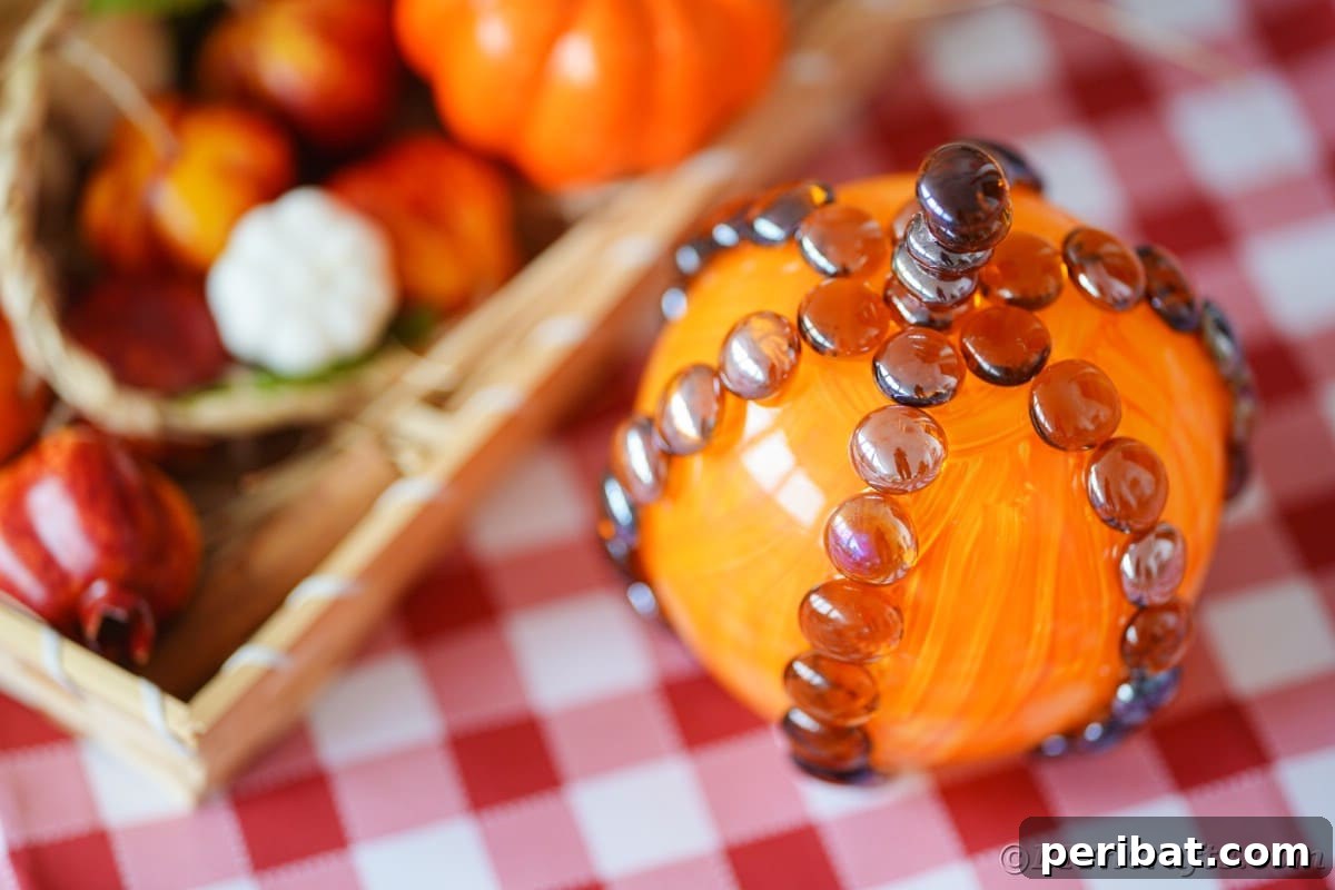 A collection of faux fall items, including leaves and small decor, rests next to a finished glass pumpkin on a wooden tray, creating a cozy autumn vignette.