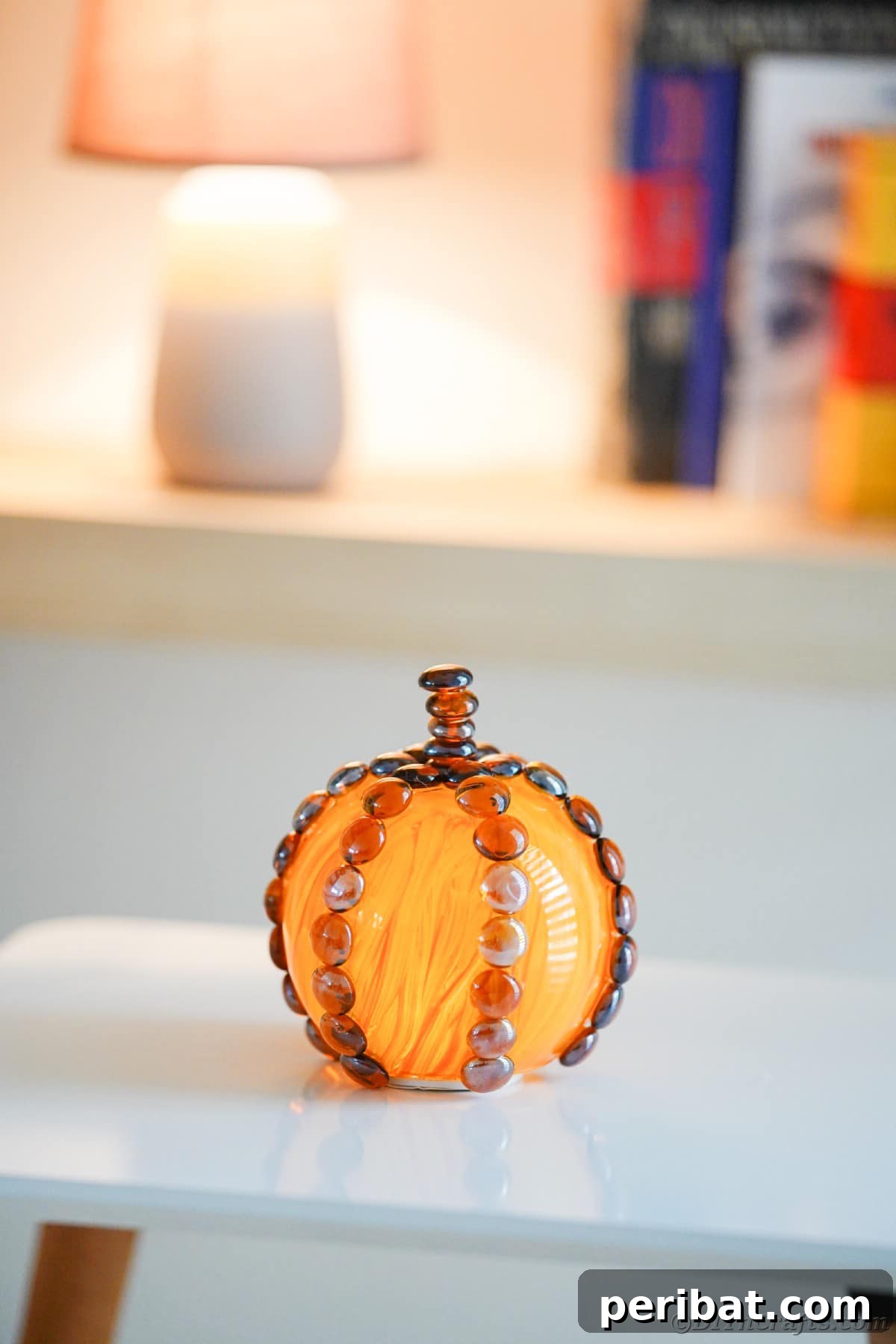 A simple glass pumpkin decoration sits on a clean white table, ready to be adorned for fall with further embellishments.