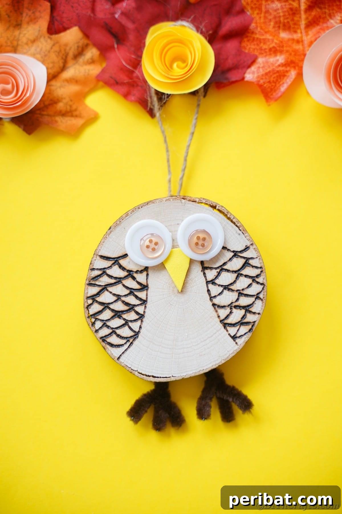 A beautifully wood-burned owl decoration, with its button eyes and detailed feather patterns, is displayed on a vibrant yellow paper background, highlighting its intricate craftsmanship.