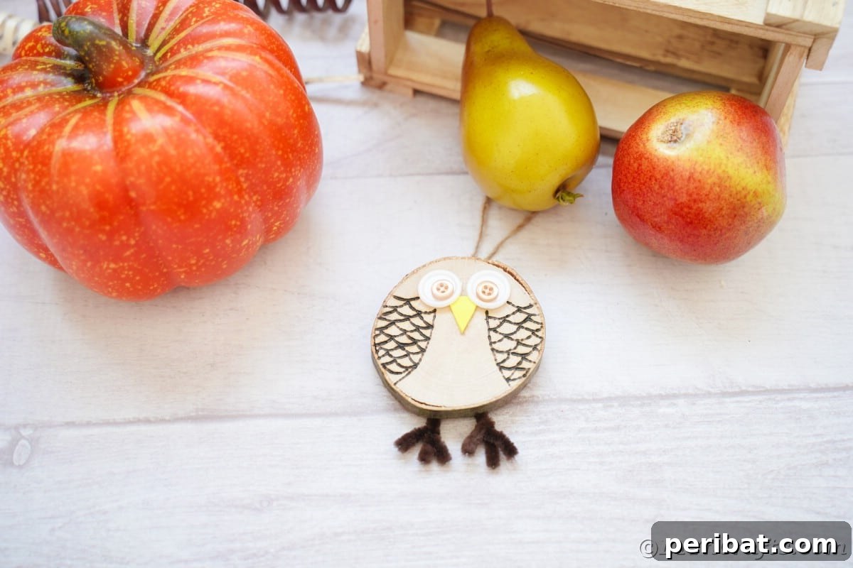 A charming wood slice owl ornament is artfully arranged on a white table, accompanied by a miniature fake pumpkin and delicate pears, creating a rustic autumn vignette.