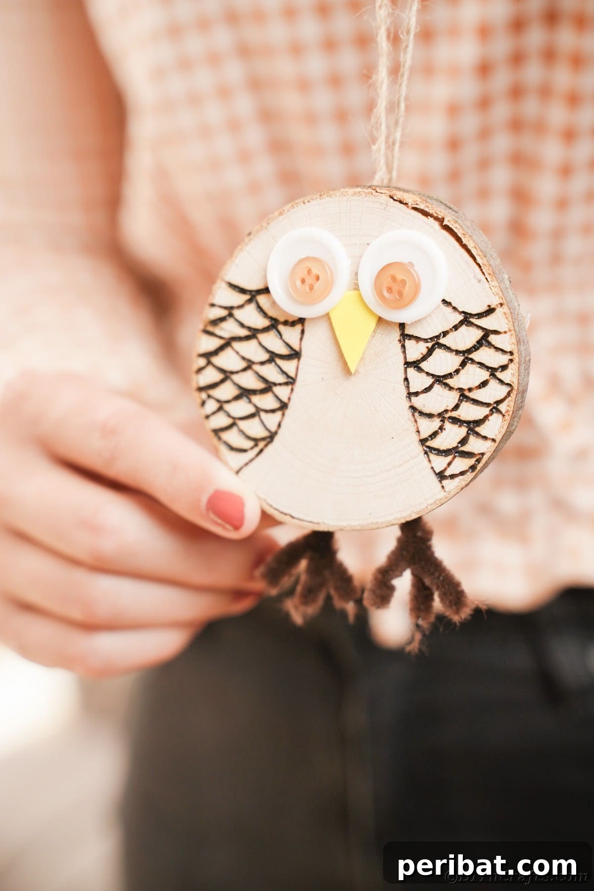 A woman in a stylish checked shirt delicately holds up a finished wood slice owl, showcasing its rustic charm and intricate wood-burned details.