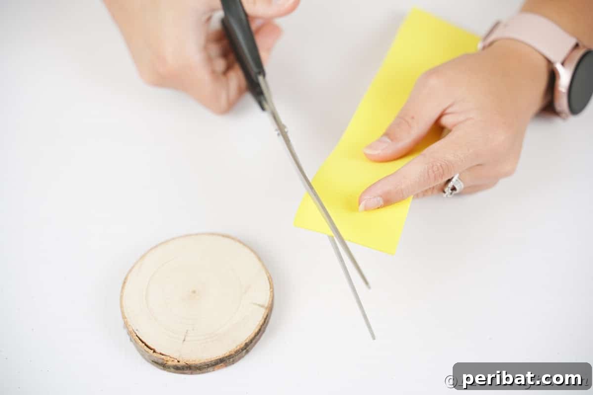 A pair of blue scissors precisely cuts a small triangle from vibrant yellow foam paper, preparing the owl's beak for the crafting project.