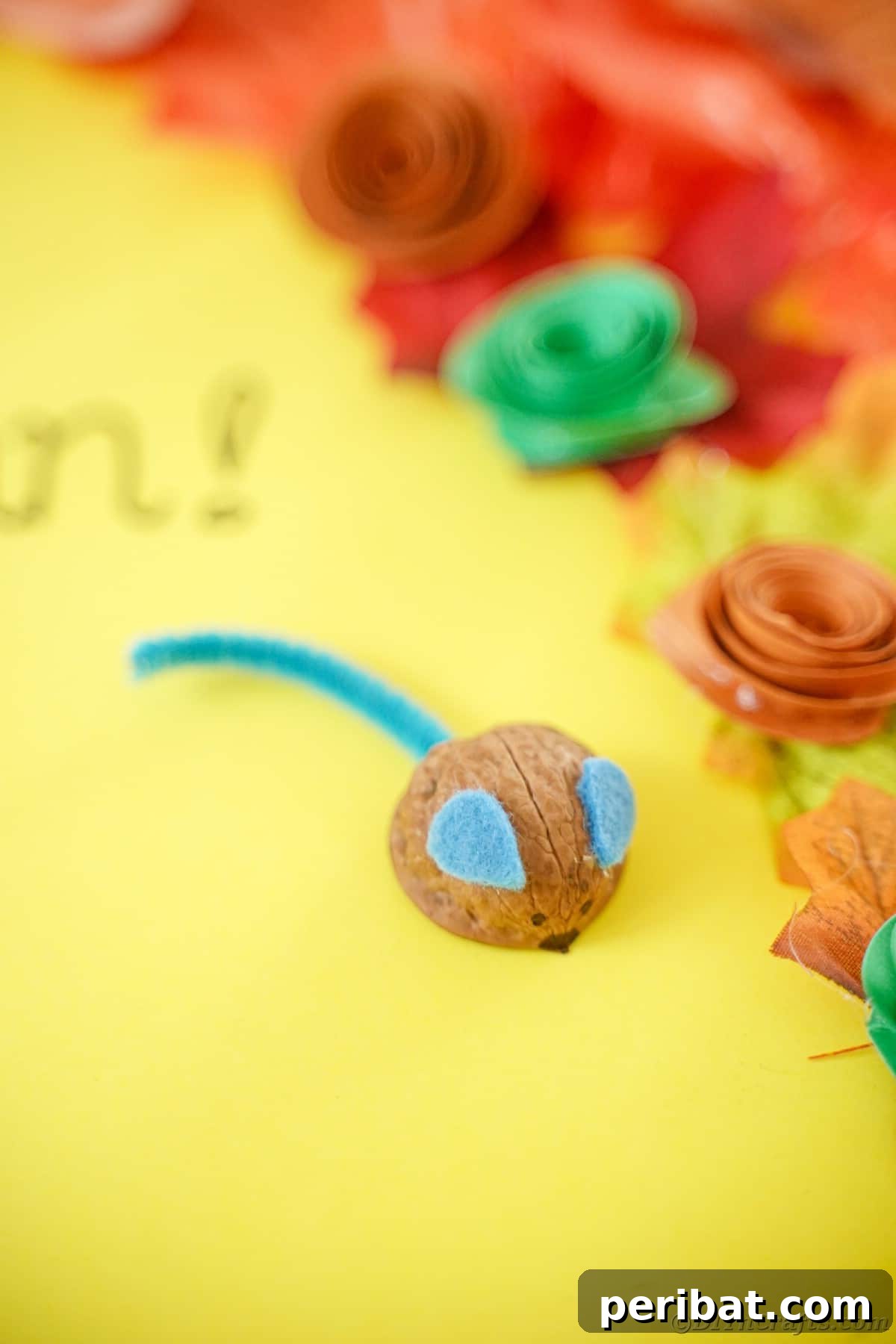 Walnut Wonders: Upcycled Shell Mouse Art 4 Walnut mouse craft displayed on yellow paper, positioned next to delicate paper flowers, creating a bright and cheerful scene.