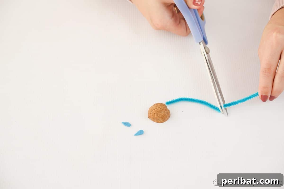 Walnut Wonders: Upcycled Shell Mouse Art 9 Scissors in action, cutting a blue pipe cleaner on a white surface, illustrating the preparation of the mouse's tail.