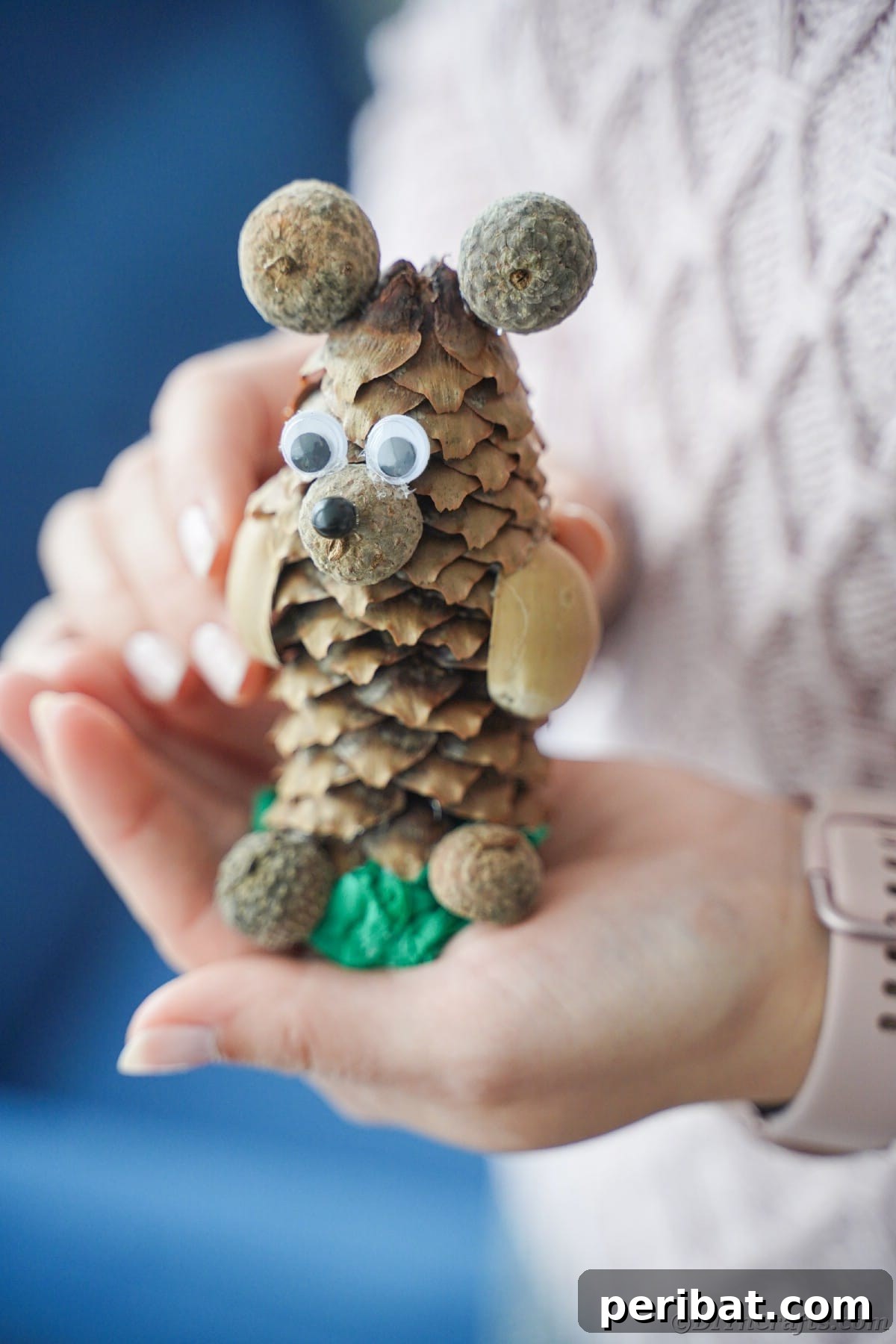 Woman in sweater holding a finished rustic pinecone bear craft