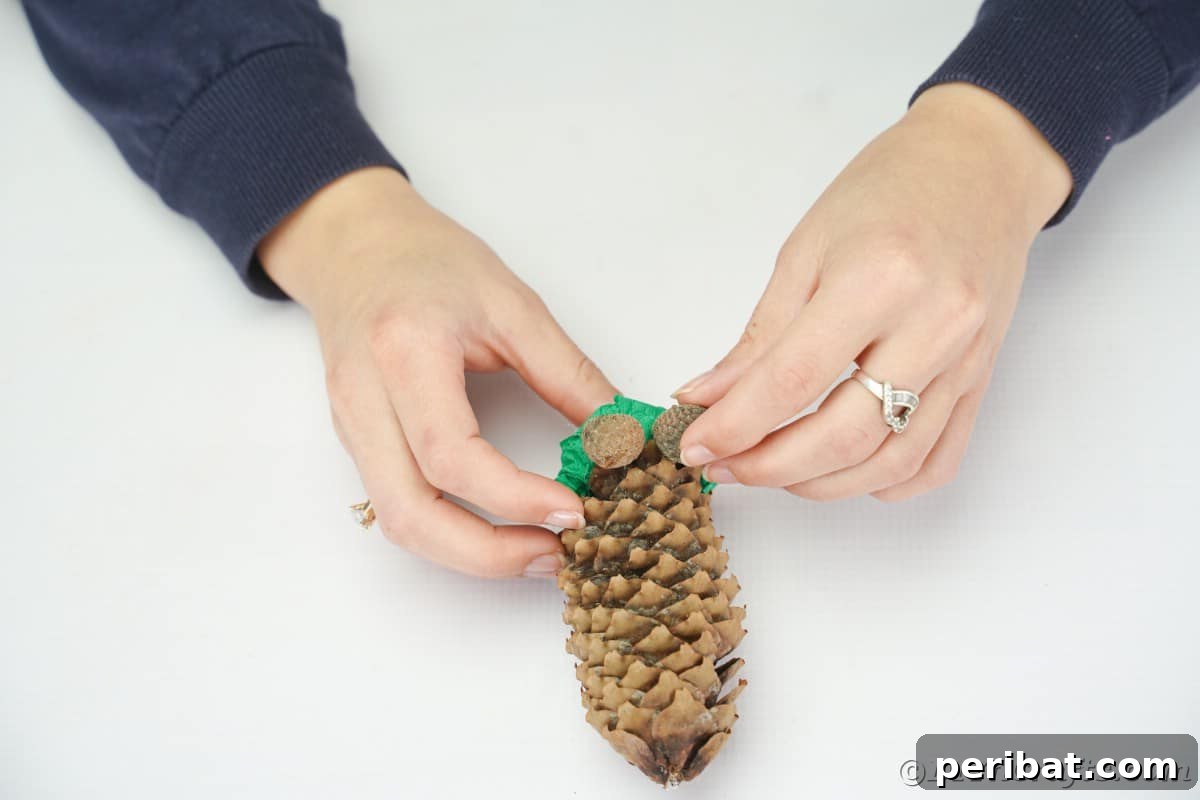 A hand gluing an acorn cap onto the bottom of a pinecone to form a foot