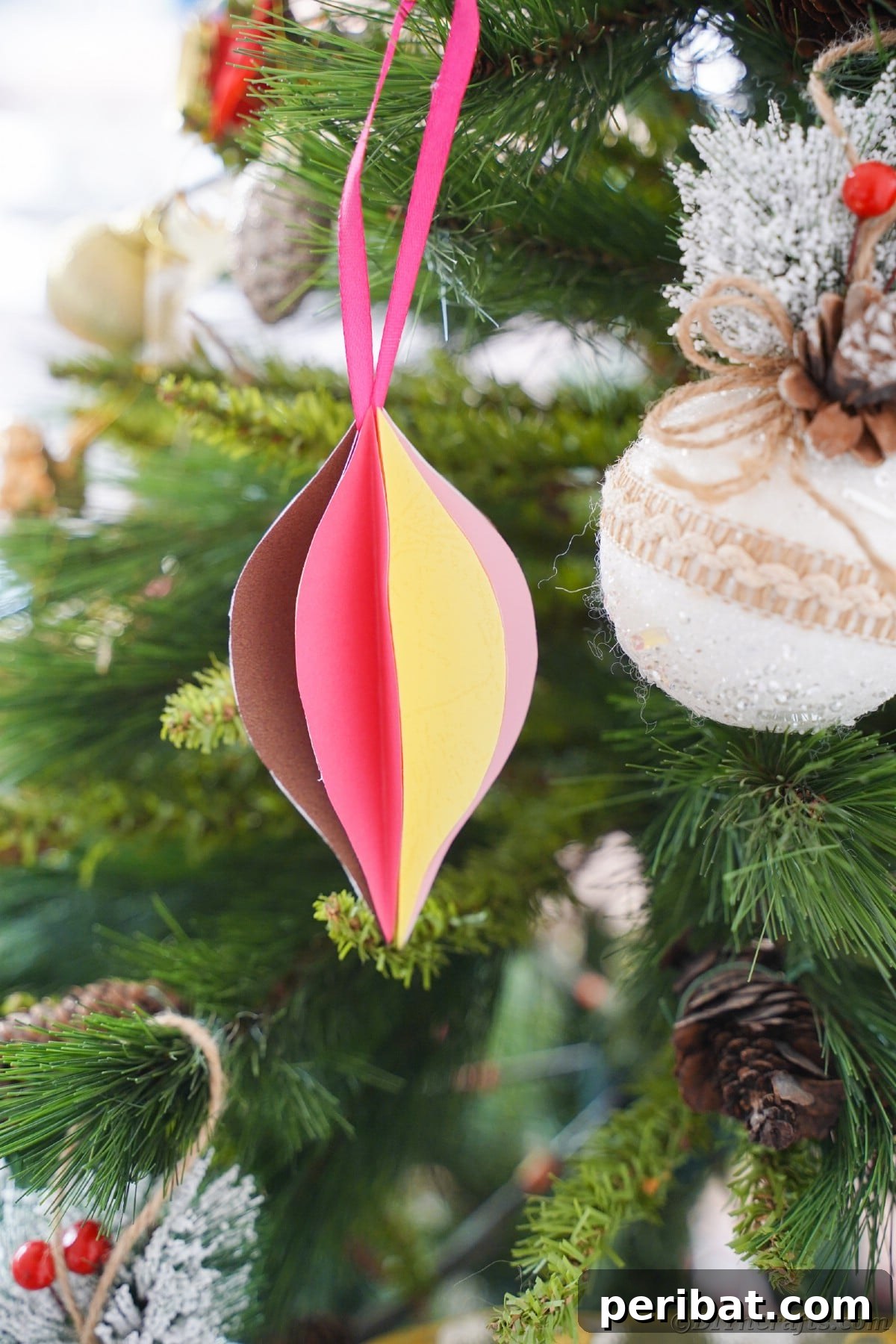 Whimsical Paper Evergreen Decor 2 Vibrantly colored teardrop paper Christmas ornament hanging elegantly on a festive tree