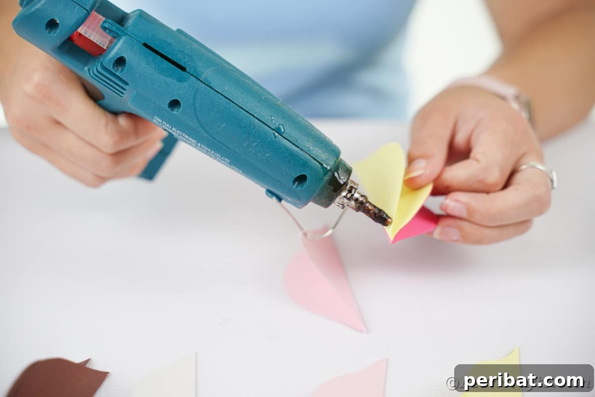 Close-up of gluing the flat sides of colored paper pieces together to form the volumetric shape of a Christmas ornament