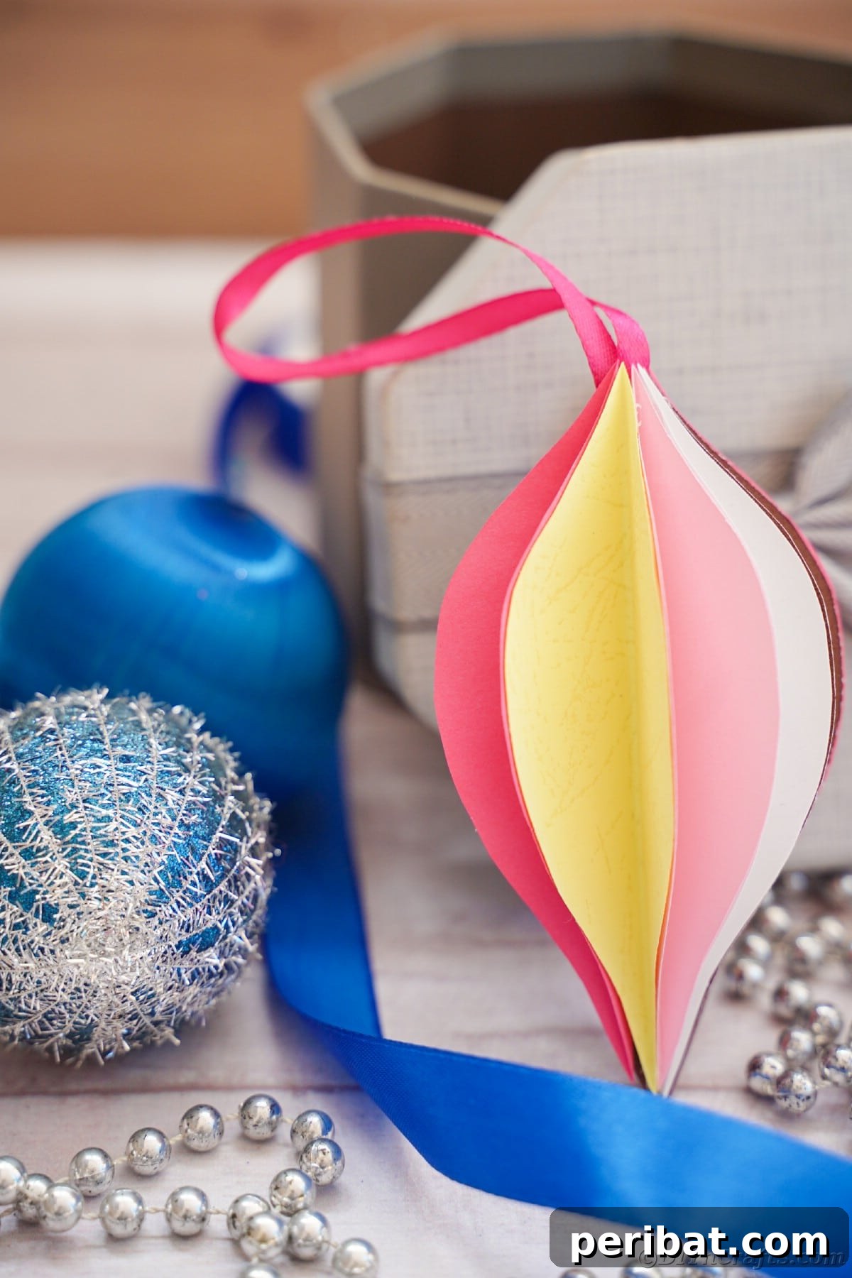 Whimsical Paper Evergreen Decor 16 A charming pink and yellow paper ornament displayed against a serene blue holiday backdrop, highlighting its festive appeal