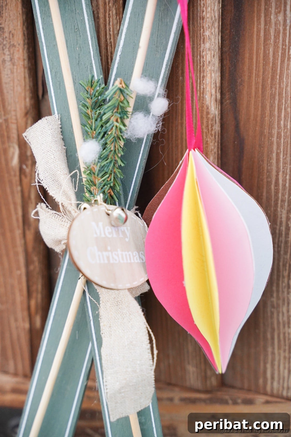 Whimsical Paper Evergreen Decor 17 A teardrop paper ornament gracefully hanging in front of miniature decorative skis with faux snow, evoking a cozy winter scene
