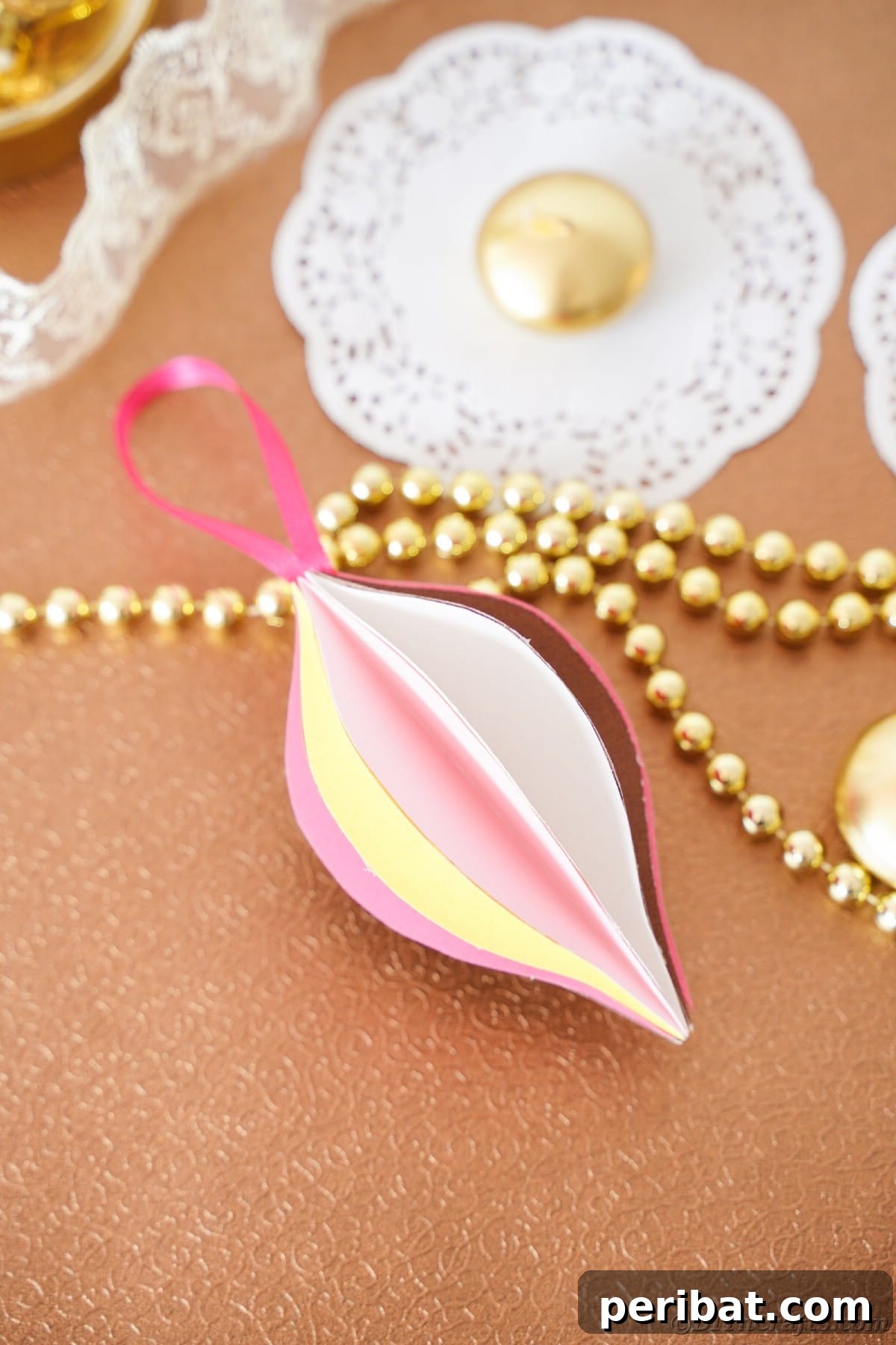 Whimsical Paper Evergreen Decor 18 A cheerful pink and yellow paper ornament resting casually on a textured brown table, perfect for rustic holiday decor