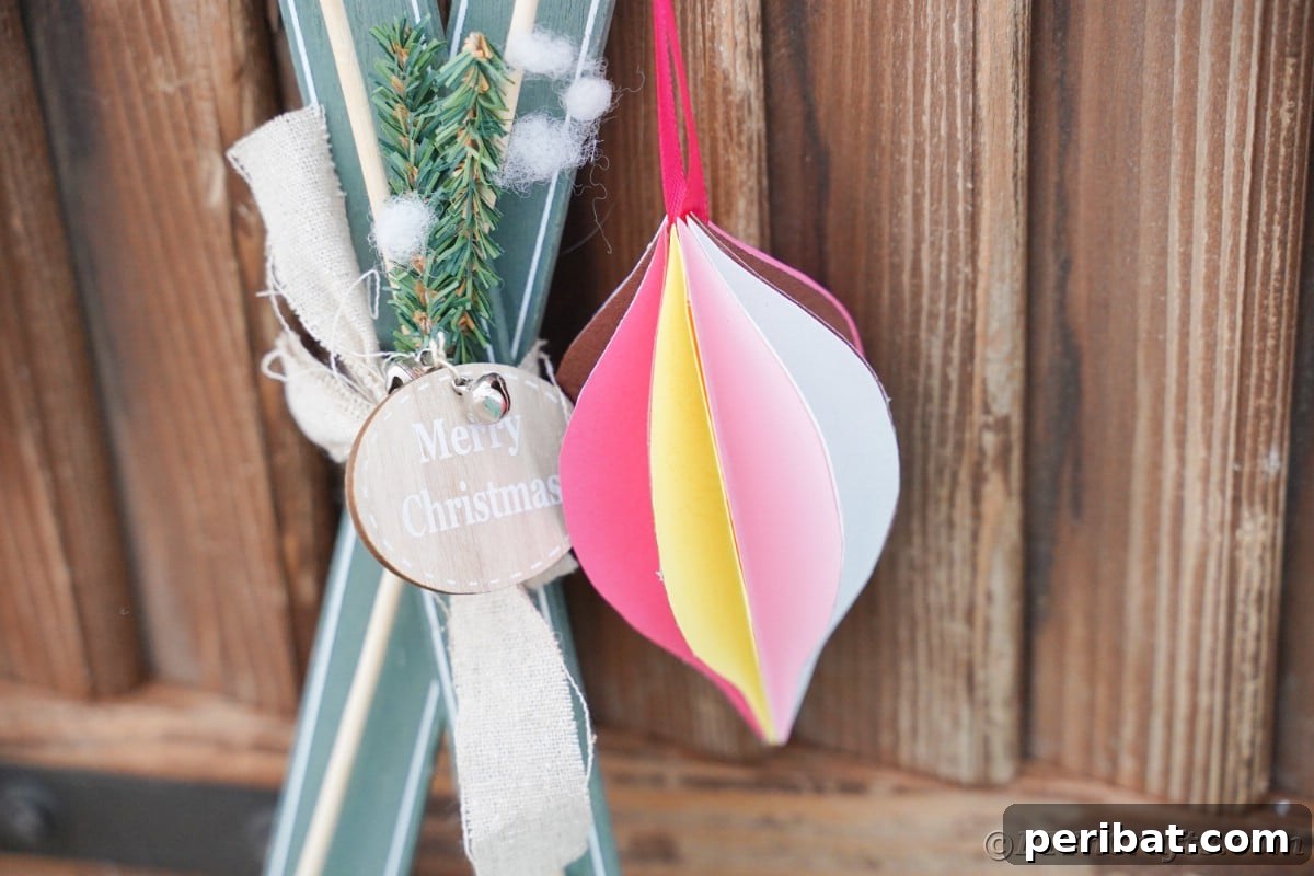 Whimsical Paper Evergreen Decor 7 A cheerful pink and yellow paper ornament suspended in front of a warm wooden background, ready for the holidays