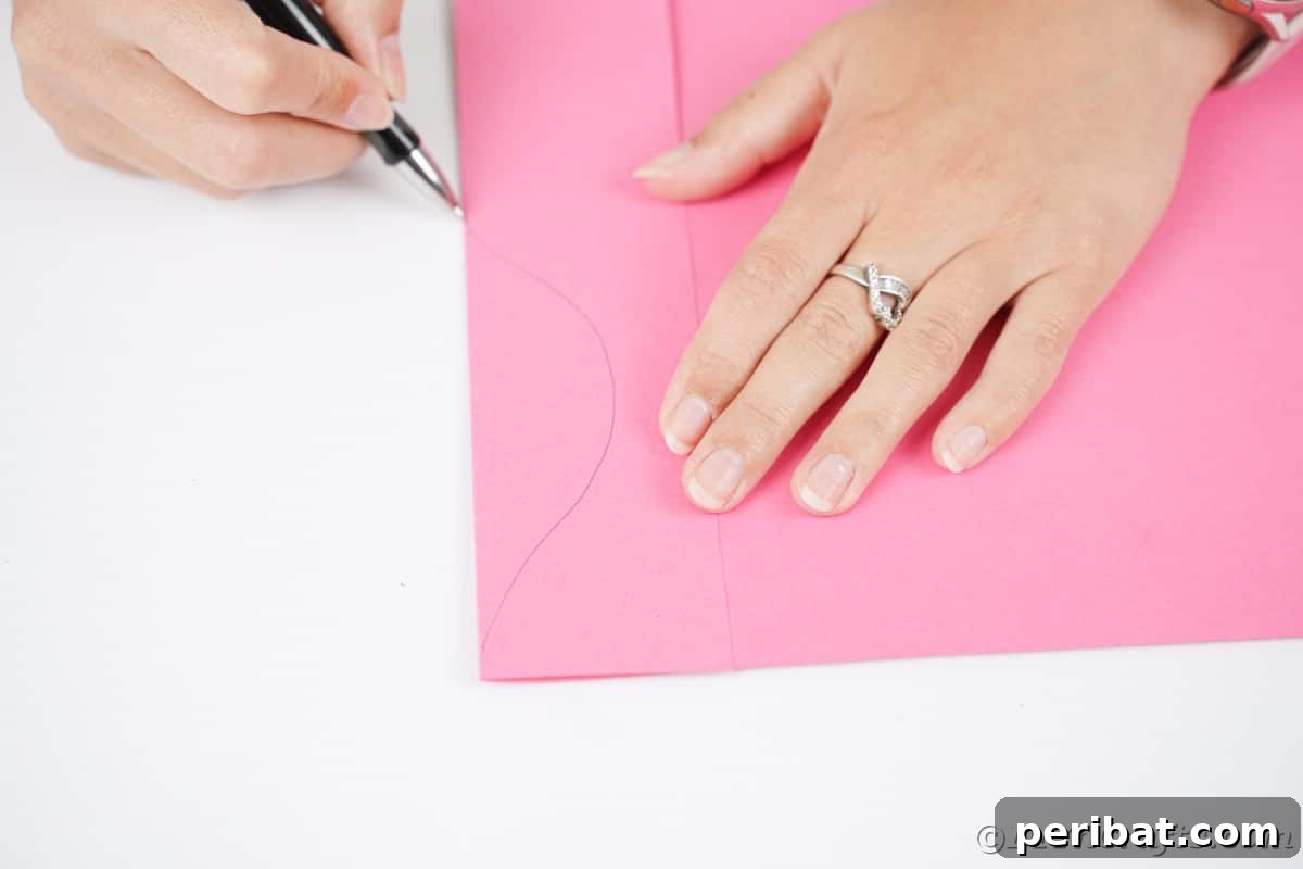 A hand carefully drawing a half-moon shape onto pink craft paper, forming the base for a Christmas ornament