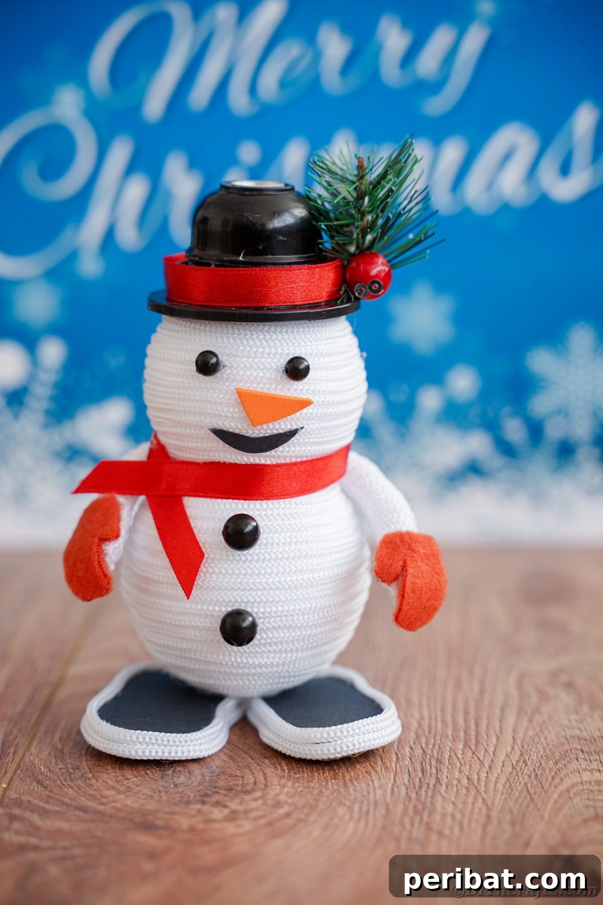 Cozy Twine Snowman Christmas Charm 2 mini snowman on table in front of blue sign that says merry christmas