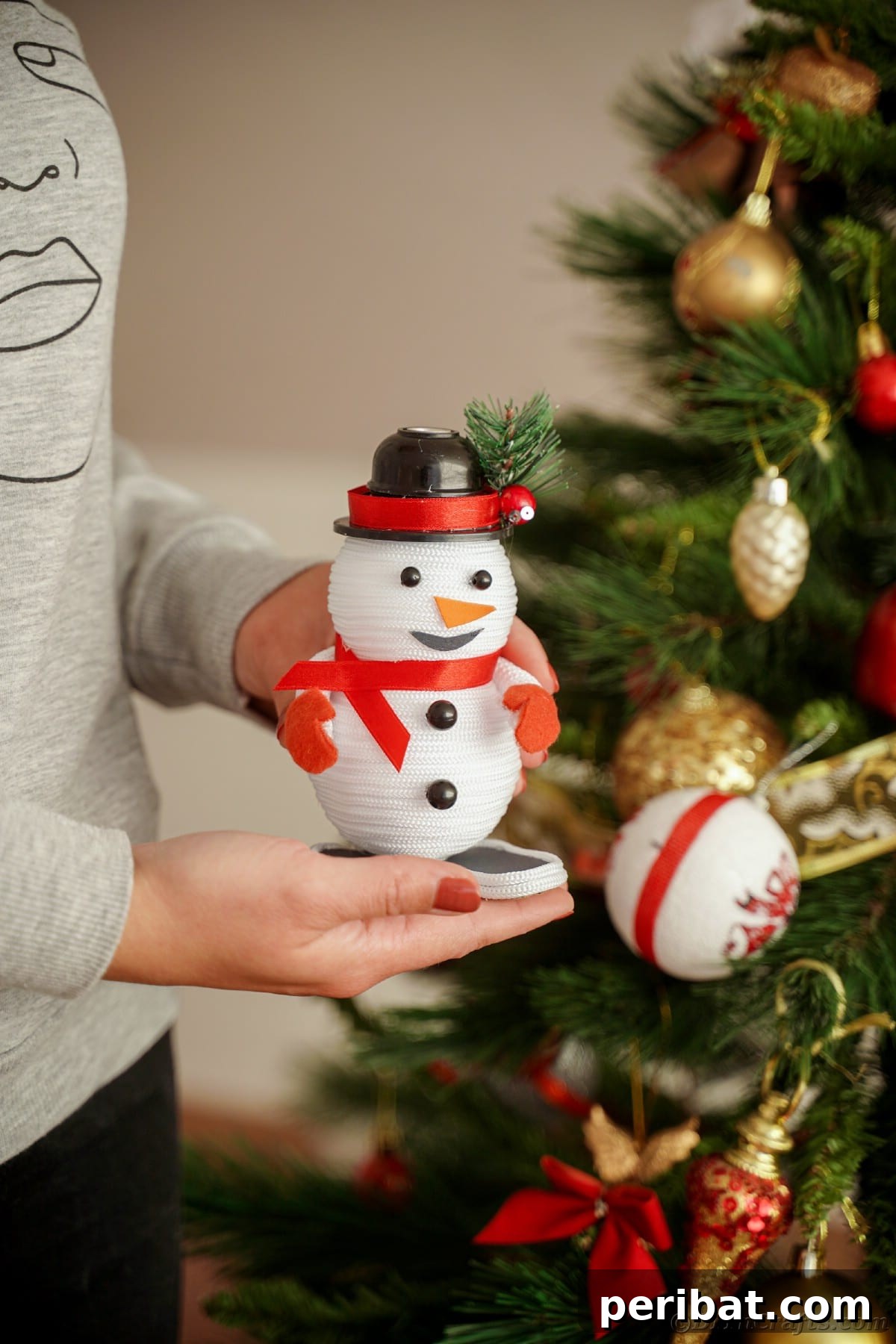 Cozy Twine Snowman Christmas Charm 25 person holding a mini snowman decoration by Christmas tree