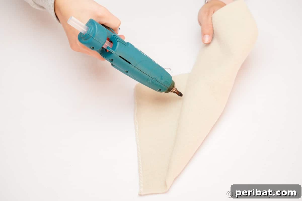 Applying hot glue along the seam of the cream felt hat to secure its conical shape.