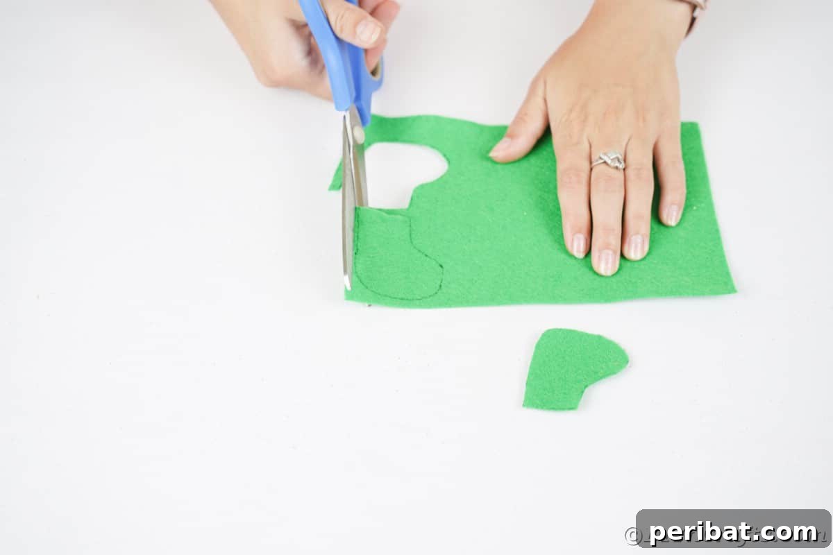 hand using blue scissors to cut out green felt boot shape