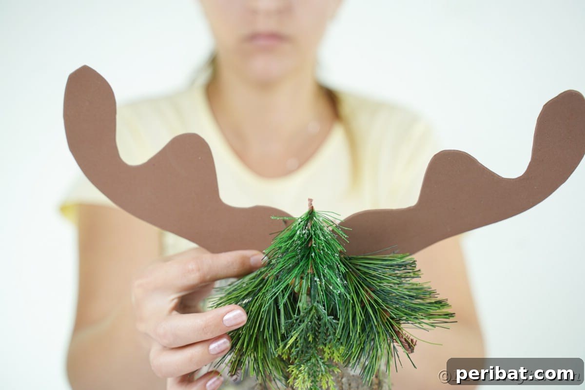 Whimsical Woodland Log Reindeer Decor 14 antlers being glued onto greenery on top of log