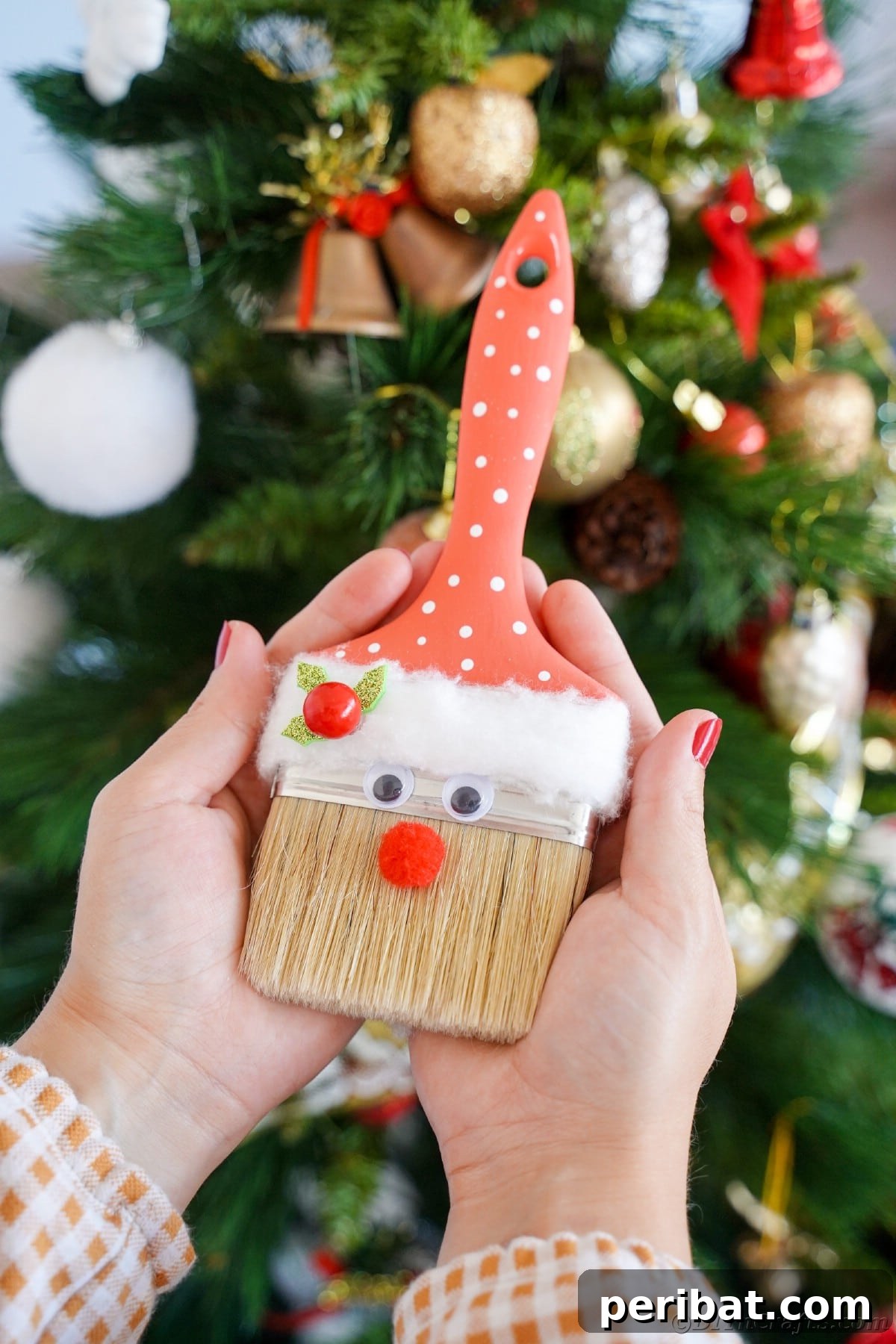 Rustic Paintbrush Santa Claus decoration held in front of a twinkling Christmas tree, highlighting its charm and ease of crafting.