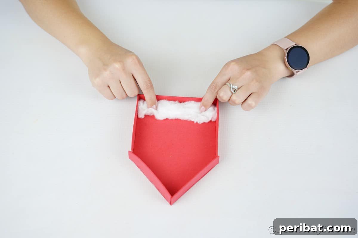 Whimsical Foam Penguin House Tree Ornament 11 Hands carefully adding soft cotton batting inside the red foam house to create a snow effect