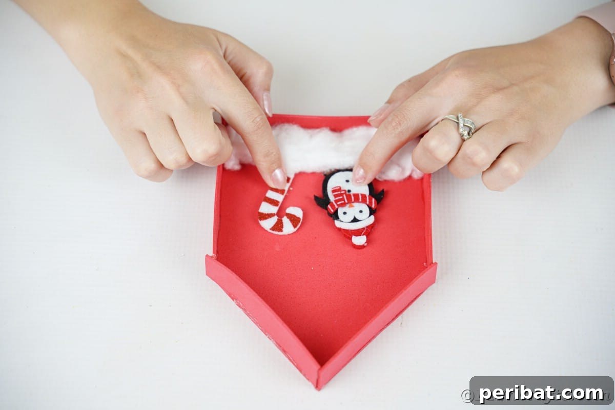 Whimsical Foam Penguin House Tree Ornament 12 Hands holding a miniature penguin and candy cane, ready to be placed inside the red foam house on the