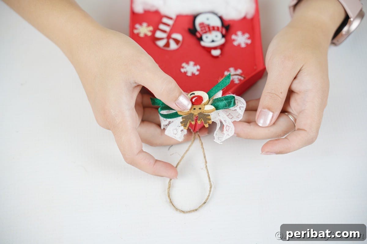 Whimsical Foam Penguin House Tree Ornament 16 A hand holding up the completed penguin house ornament, featuring a reindeer face on top of the bow