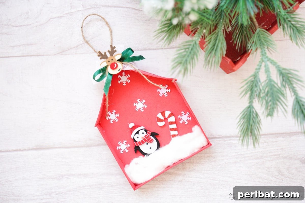 Whimsical Foam Penguin House Tree Ornament 3 A red foam penguin house ornament displayed on white shiplap next to festive greenery and berries, creating a cozy winter scene
