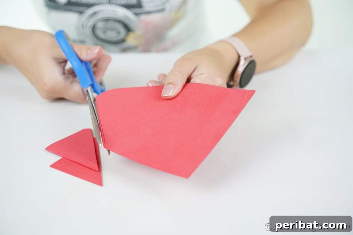 Whimsical Foam Penguin House Tree Ornament 9 A person using blue scissors to precisely cut a red house shape out of foam paper