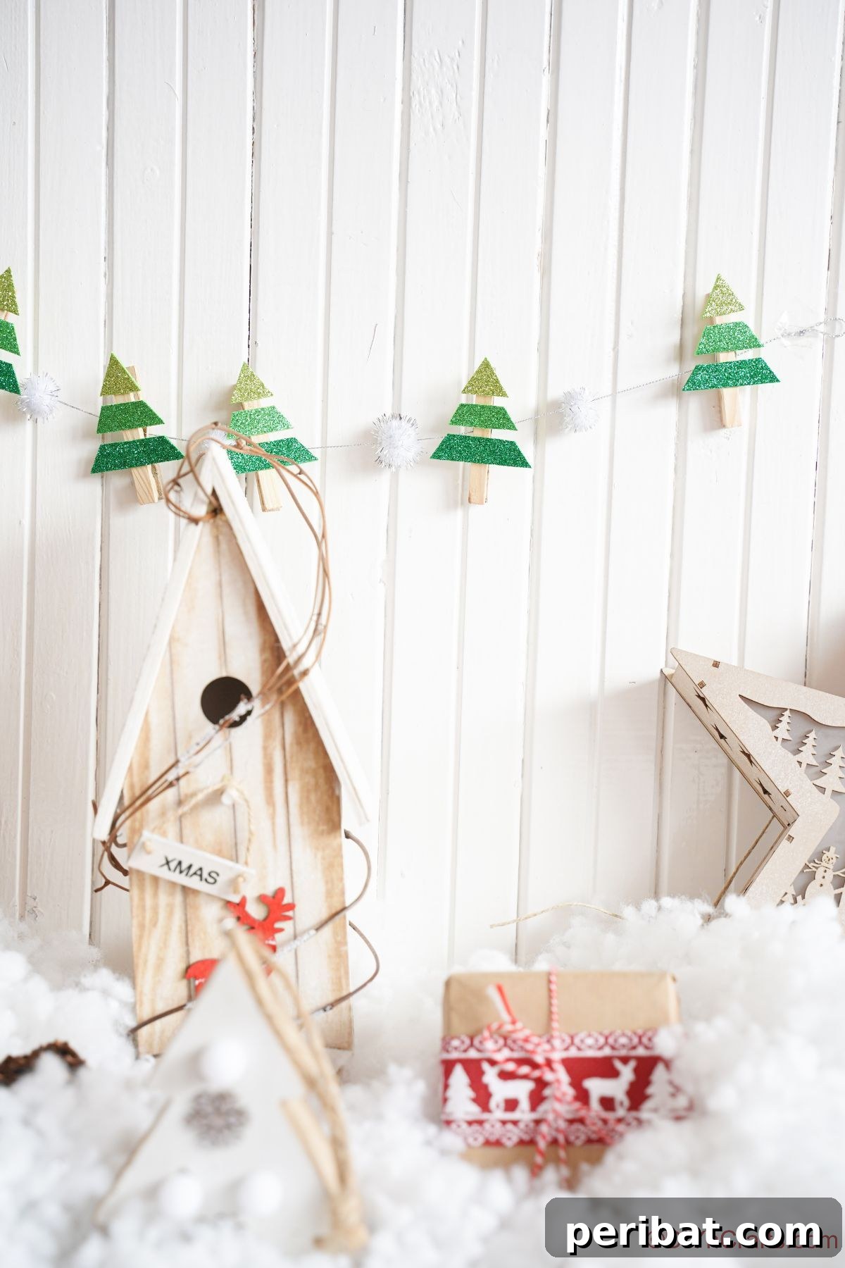 mini tree garland hanging on white wall above holiday decor and fake snow