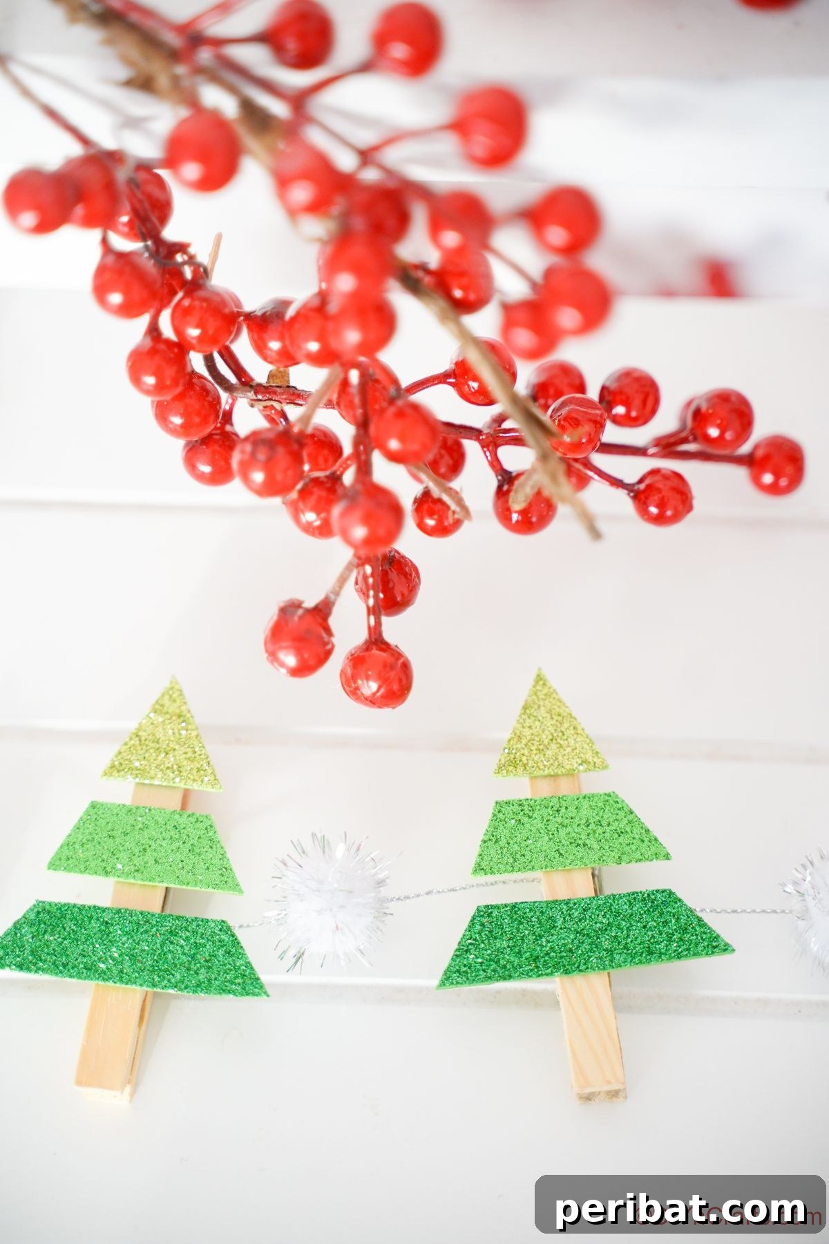 two clothespin mini trees on white shiplap with red fake berries hanging above