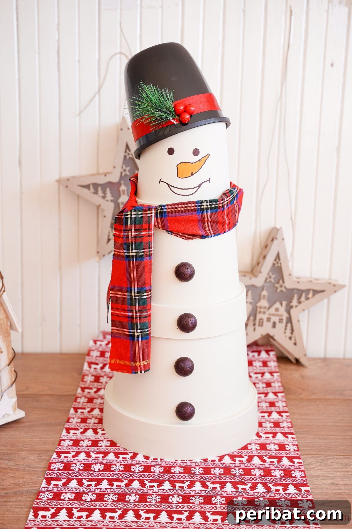 Charming white flower pot snowman with a plaid scarf and black top hat, sitting on holiday paper