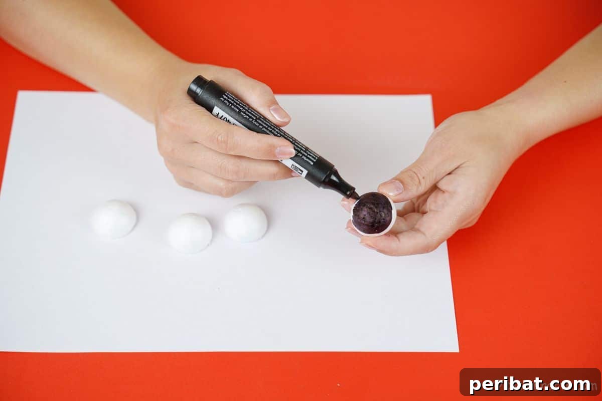 Hand coloring the rounded half of a styrofoam ball black with a permanent marker for snowman buttons