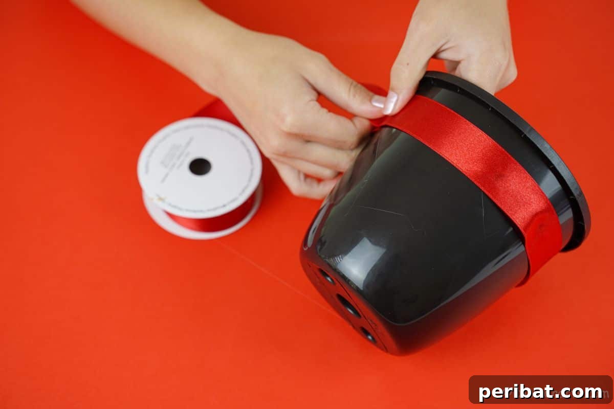 Close-up of a hand carefully gluing red ribbon around the rim of a black bucket to create a hat brim