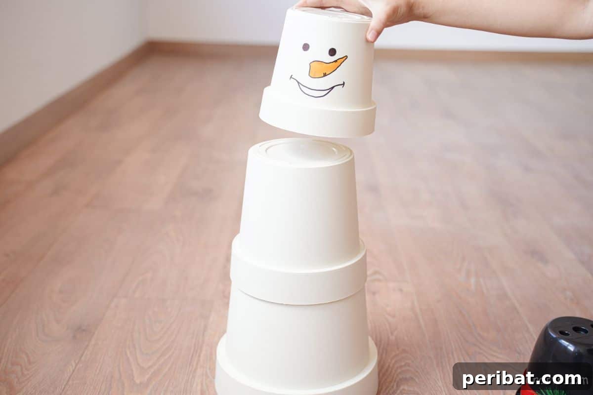 Hand carefully stacking white flower pots in decreasing size, with the top pot already featuring a snowman face