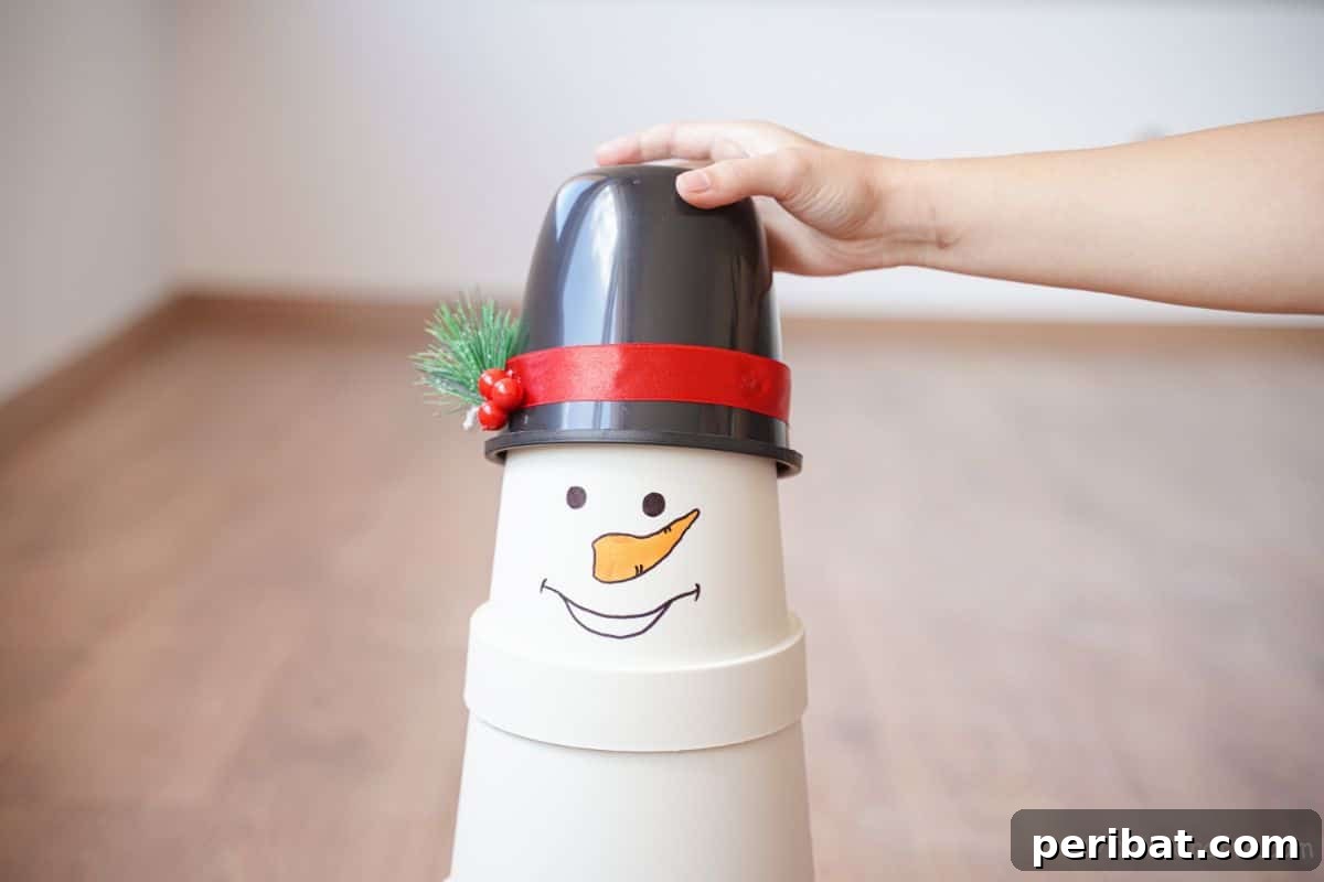 Hand positioning a black bucket hat at an angle on top of the assembled flower pot snowman