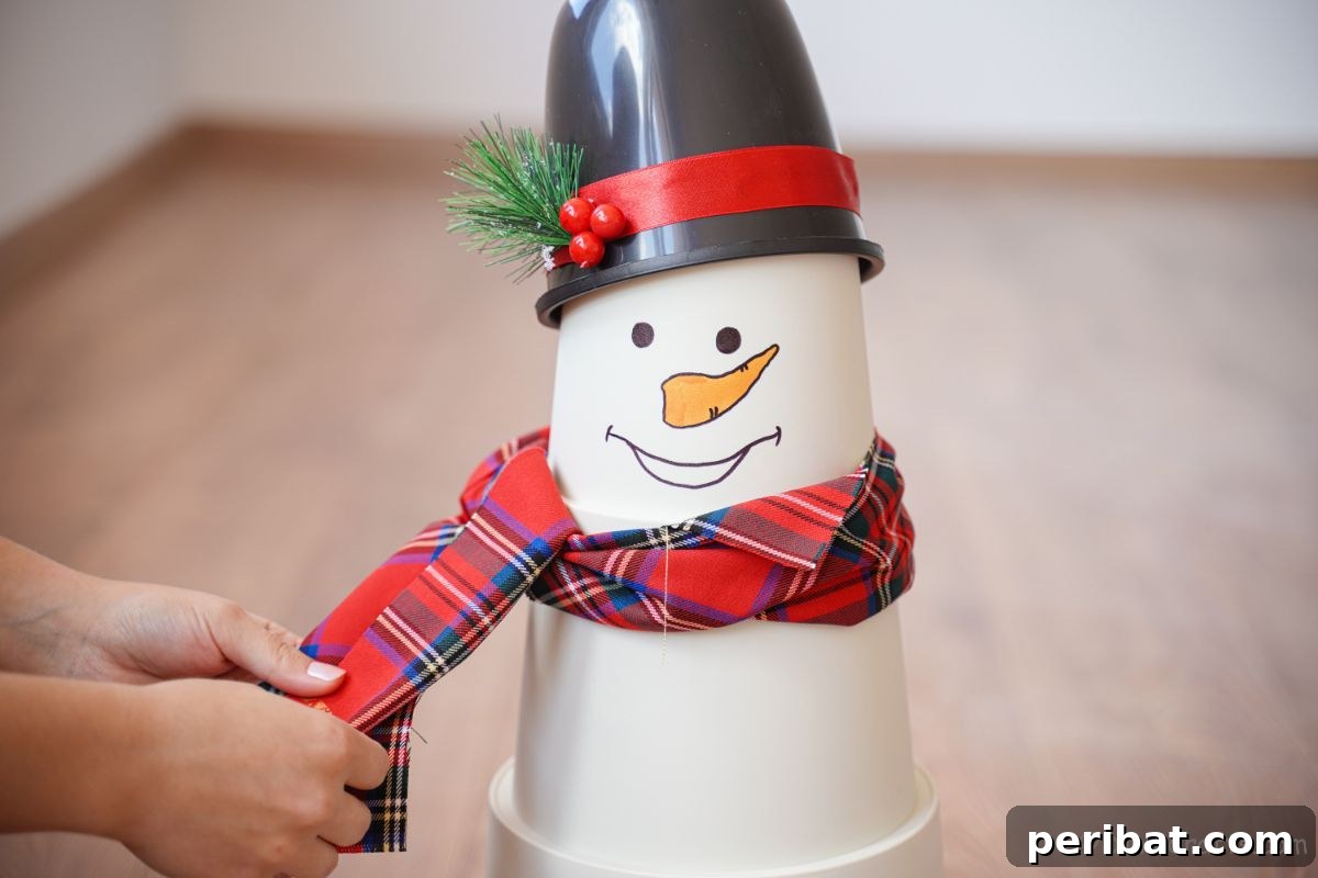 Hands tying a cozy plaid scarf around the neck of a white flower pot snowman