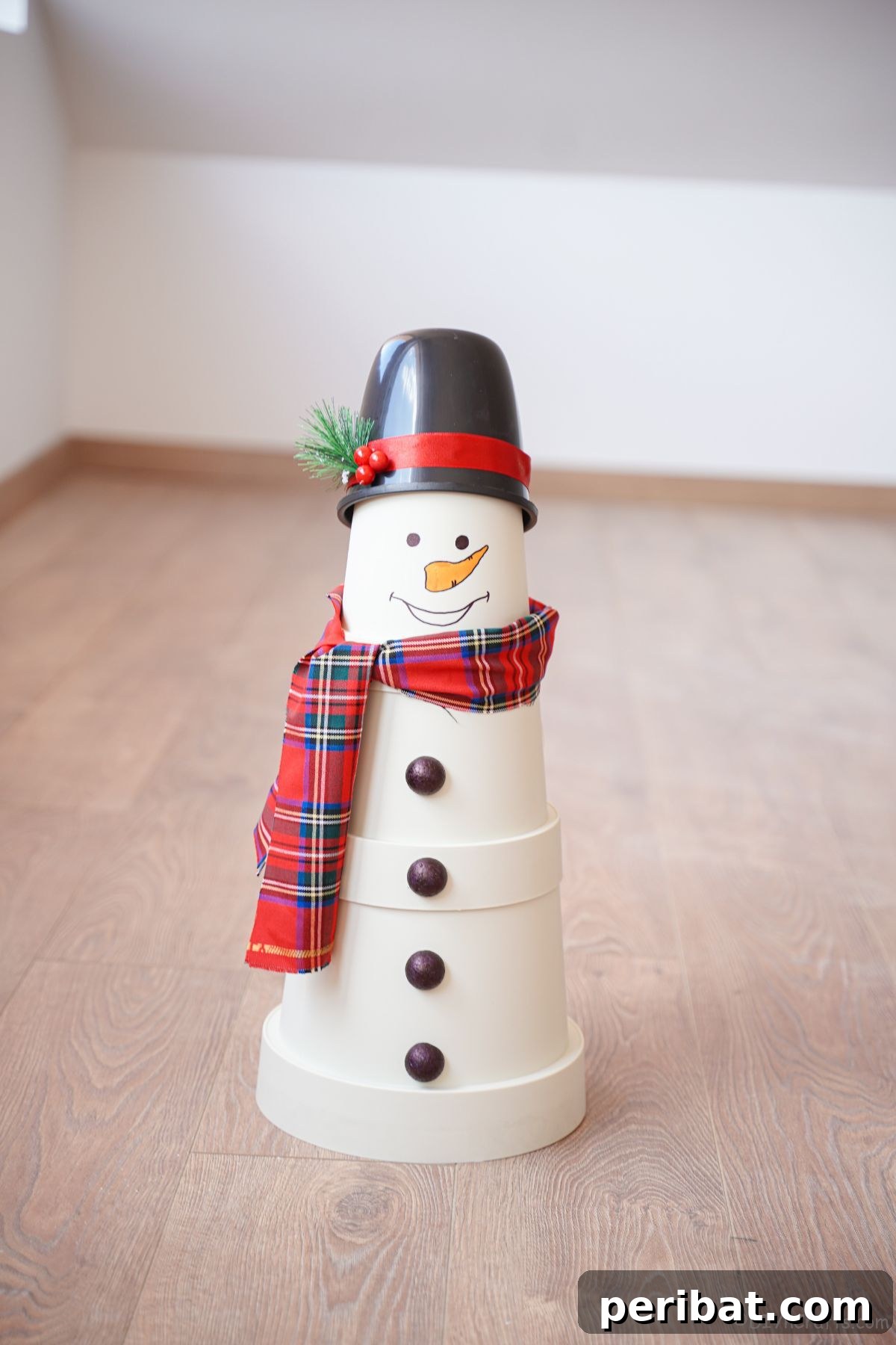Elegantly crafted white flower pot snowman wearing a festive plaid scarf and a chic black top hat, positioned on a wooden floor