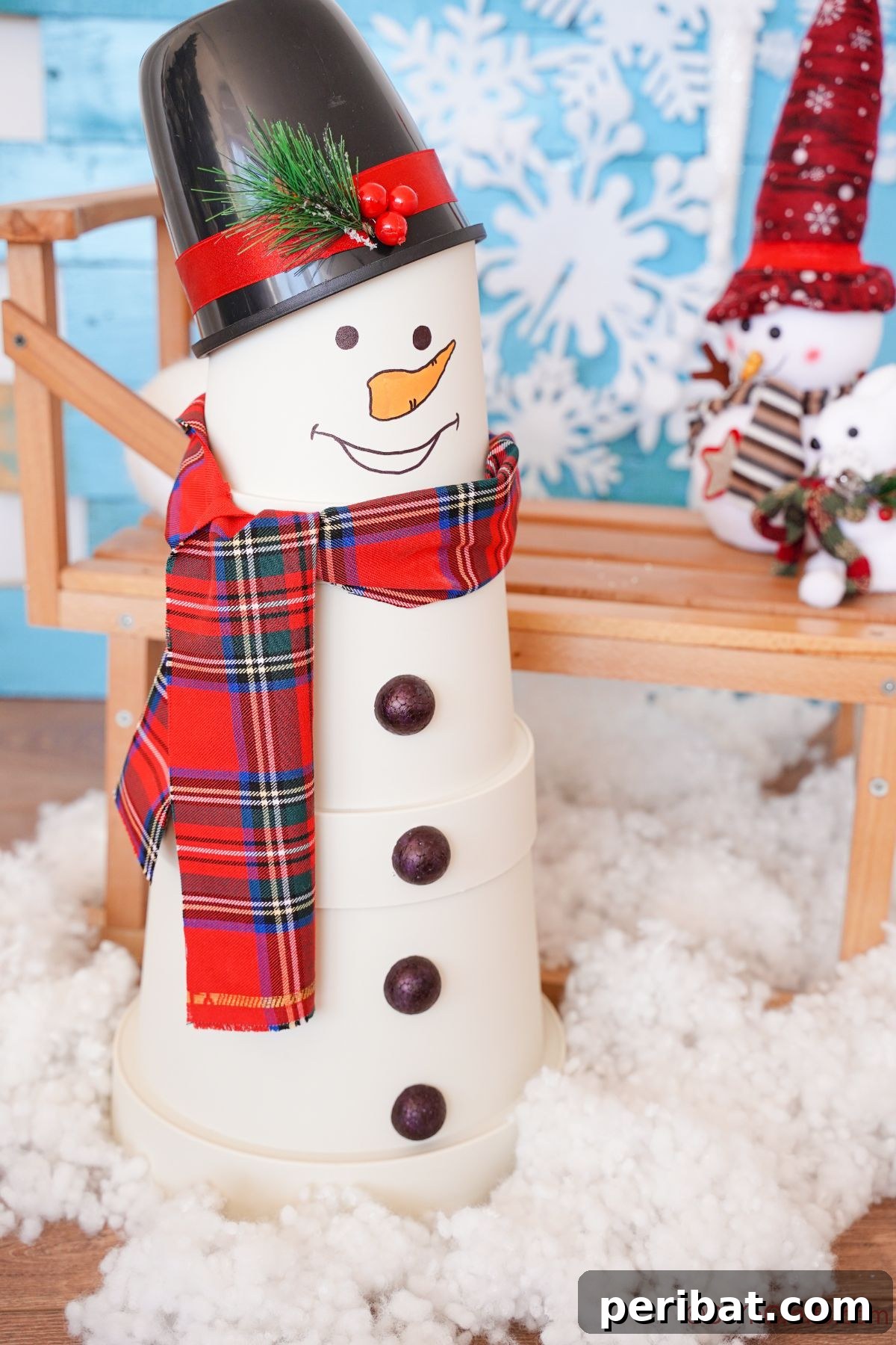 A charming white flower pot snowman positioned on fake snow in front of a quaint wooden bridge