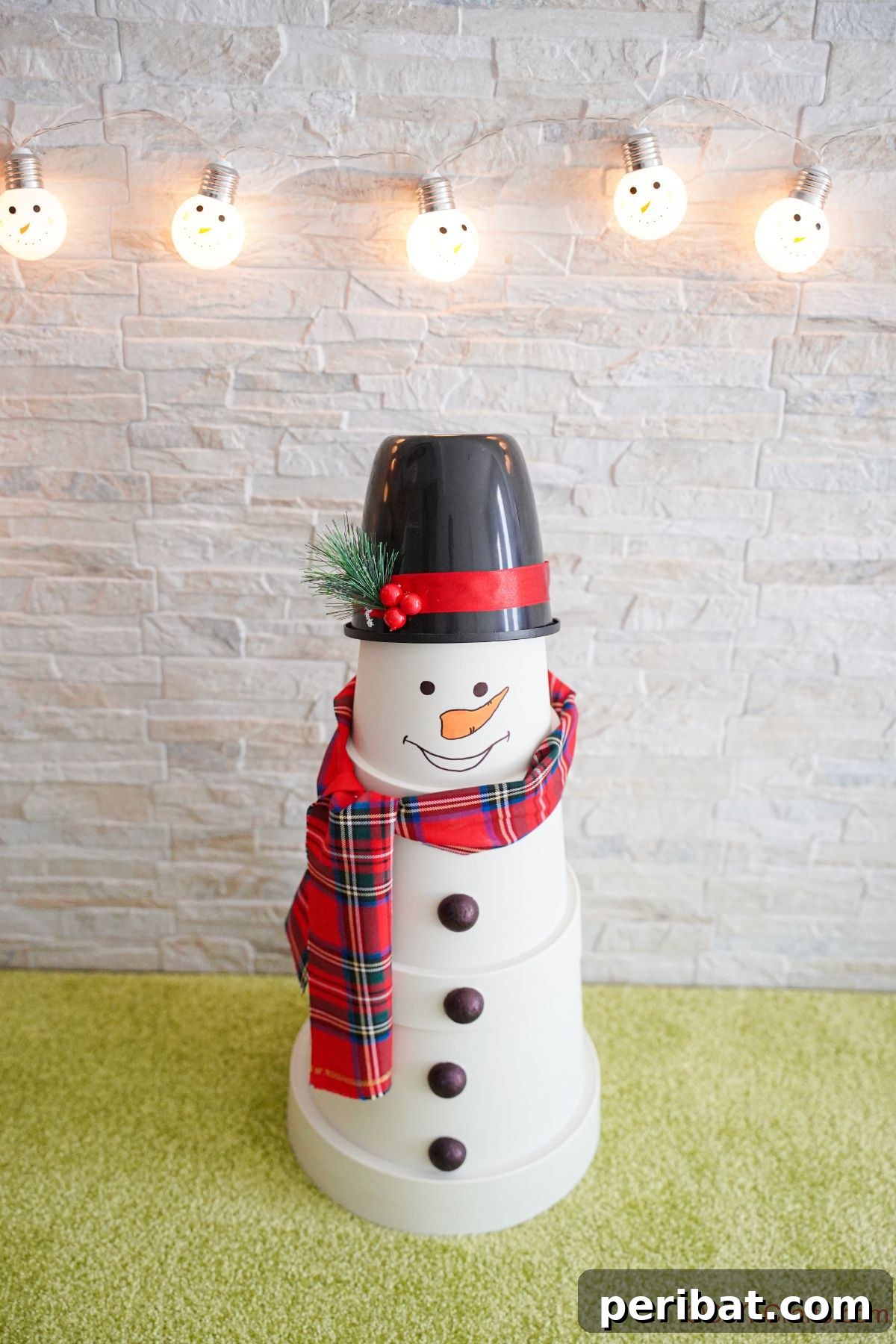 A beautifully decorated fake snowman on a green floor, with a white brick wall background adorned with twinkling lights