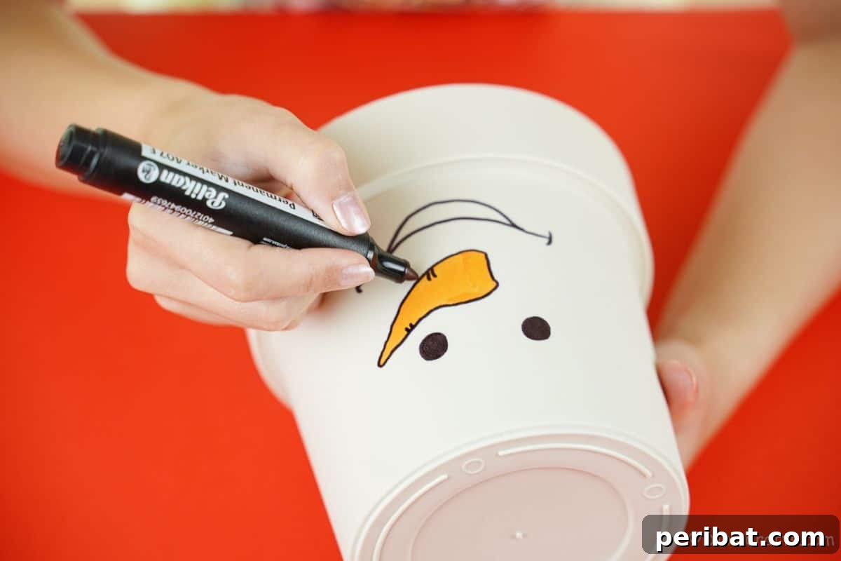Detailed shot of a hand outlining an orange carrot nose with a black marker on a white flower pot