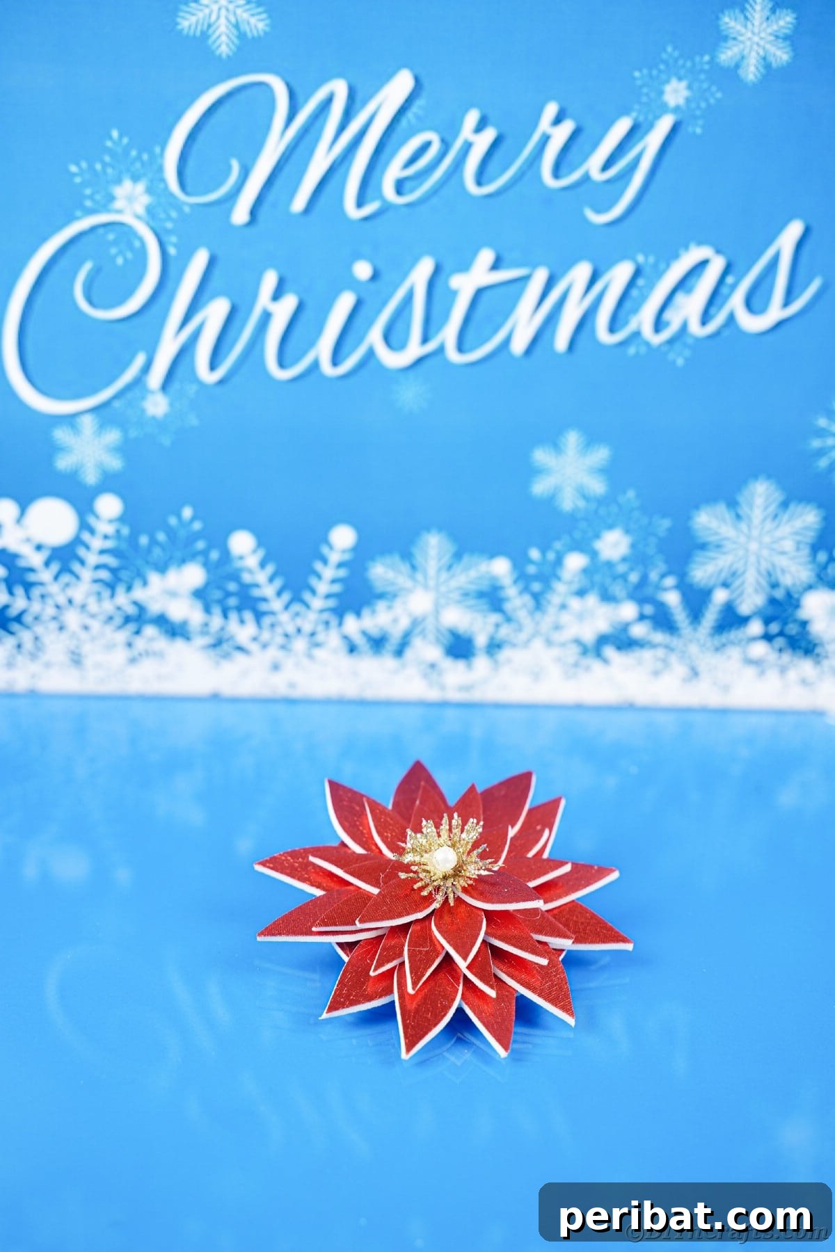Craft Your Own Foam Poinsettia Brooch or Festive Ornament 6 Fake poinsettia flower on blue table in front of white merry christmas sign
