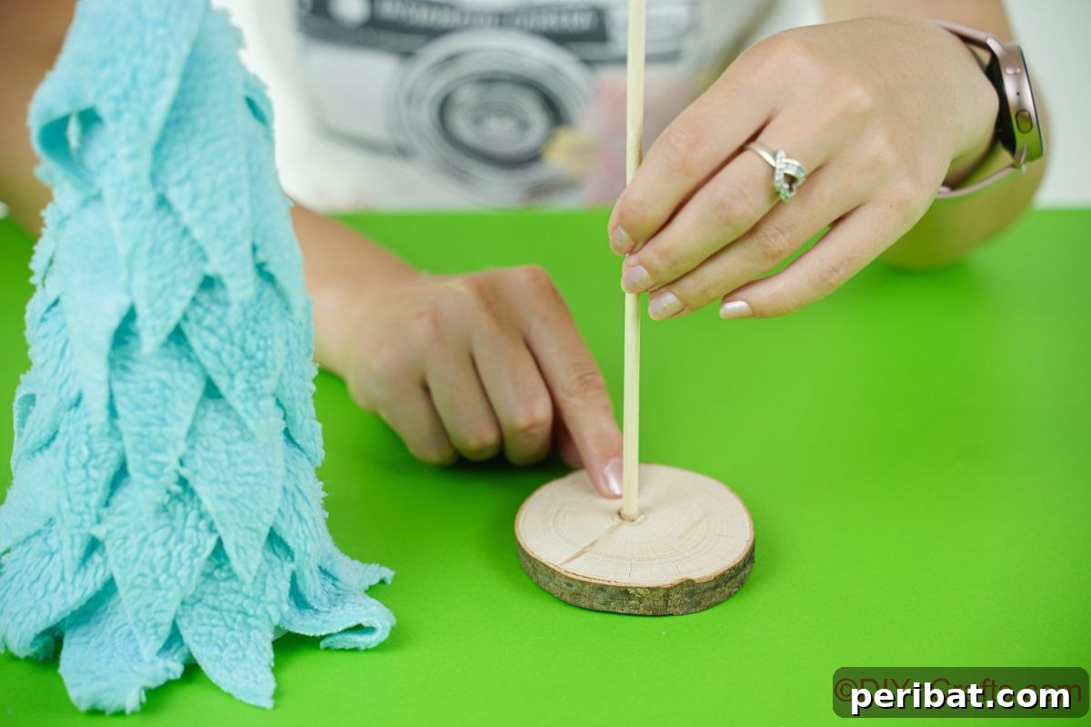 Cozy Upcycled Sweater Christmas Tree 13 hand holding a dowel onto a wood slice next to blue fabric christmas tree