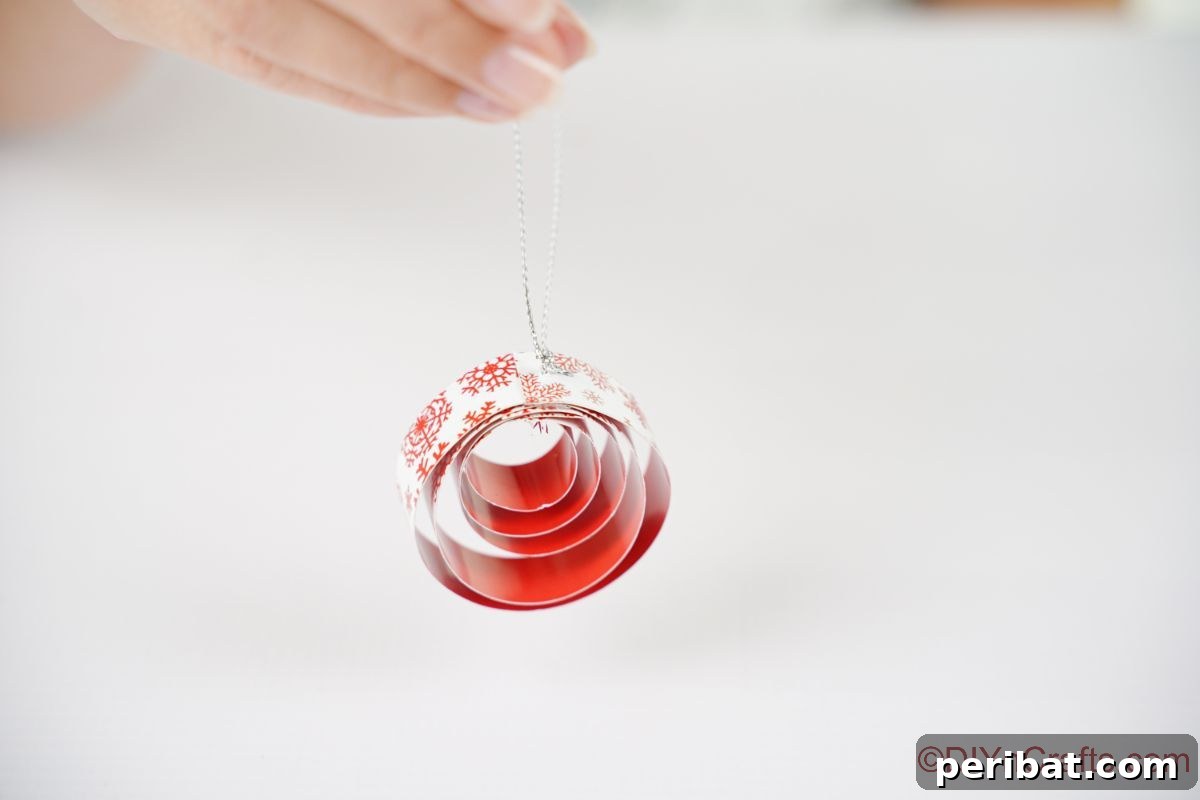 Layered Rolled Paper Christmas Charm 14 hand holding round red and white paper ornament above white table